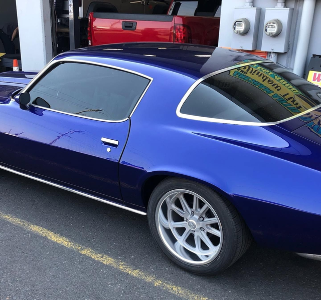Blue classic car with tinted windows parked beside a garage wall