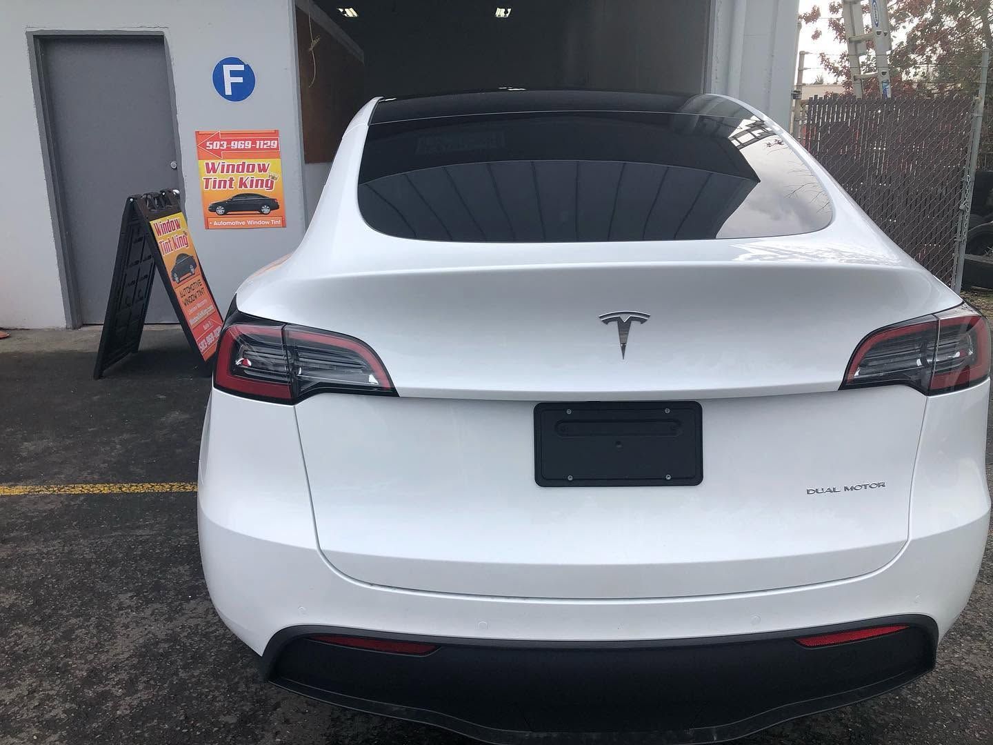 Rear view of a white Tesla parked beside a building with a charging station.