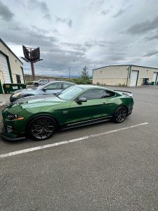 Dark green sports coupe parked in an industrial lot under cloudy skies