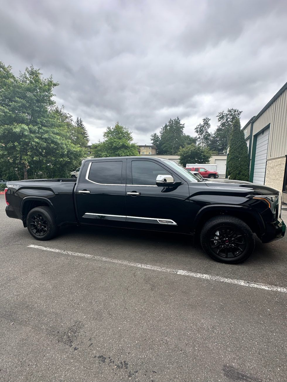 Black pickup truck parked in a lot beside a building under cloudy skies
