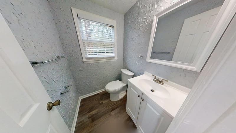 Bathroom after restoration with new white vanity, wood-look flooring, and clean textured walls