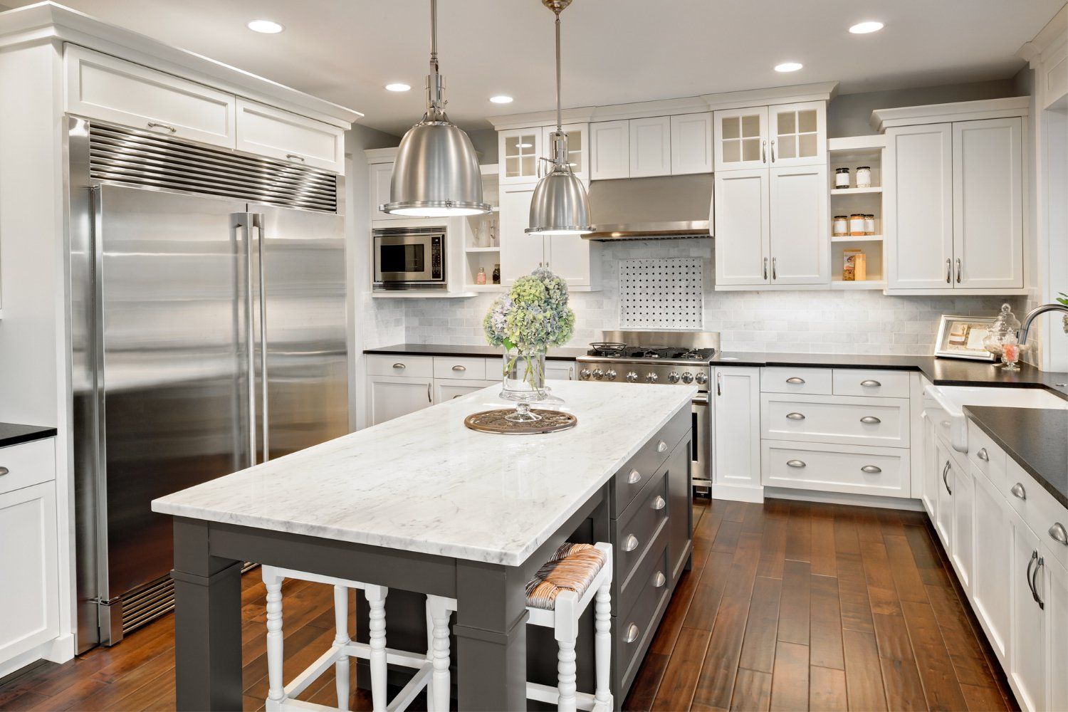 Spacious white kitchen with a gray island, stainless steel appliances, and dark wood floors.