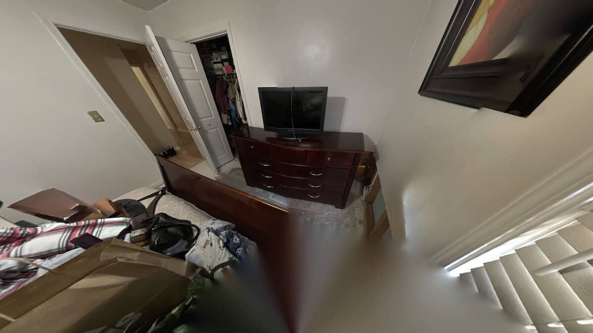 A cluttered bedroom with a dresser, TV, open closet, and bed. The room appears small with white walls and a window.