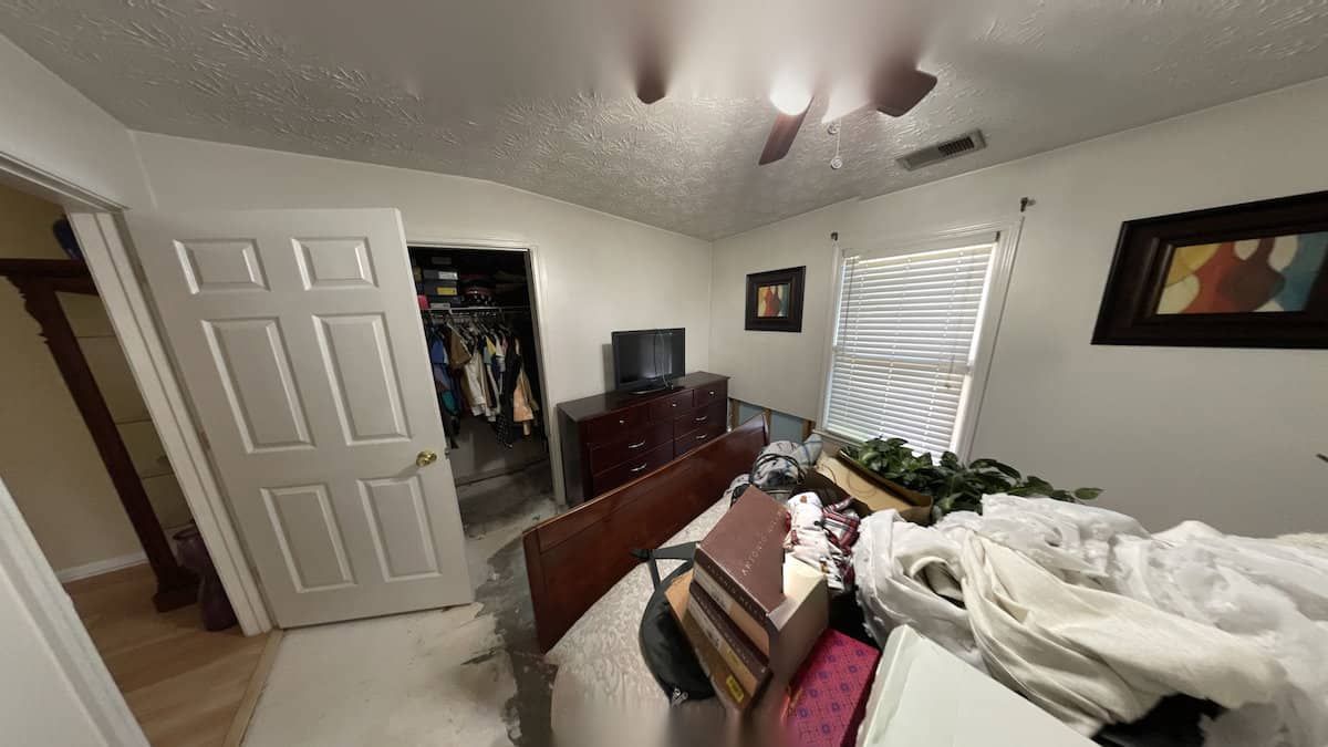 Cluttered bedroom with an open closet, door, and items on the bed and dresser. Ceiling fan visible.