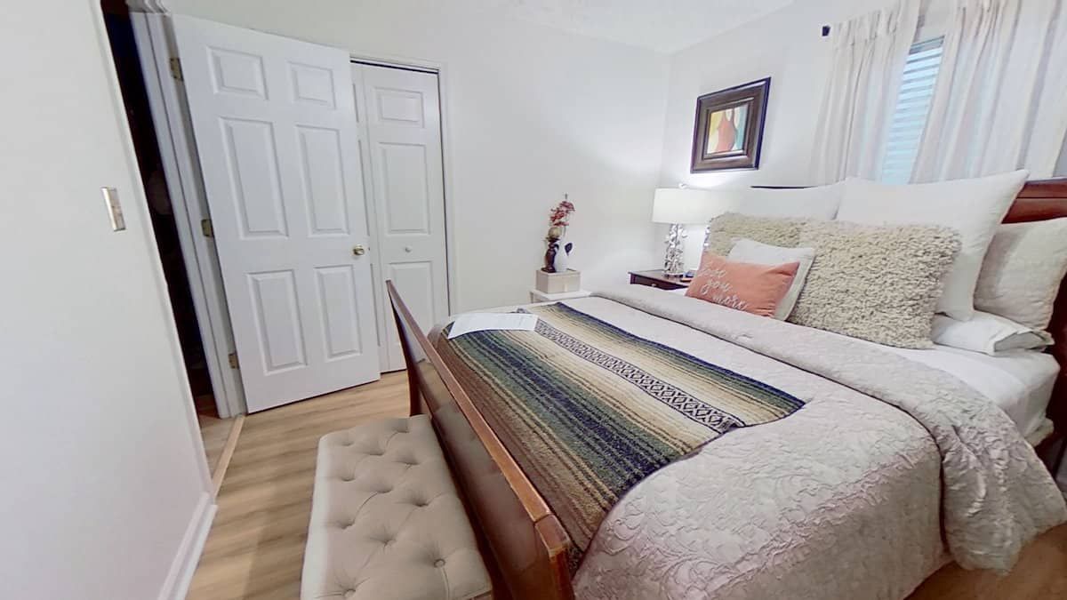 Bedroom with wooden bed, white bedding, a bench, closet, and a small artwork.