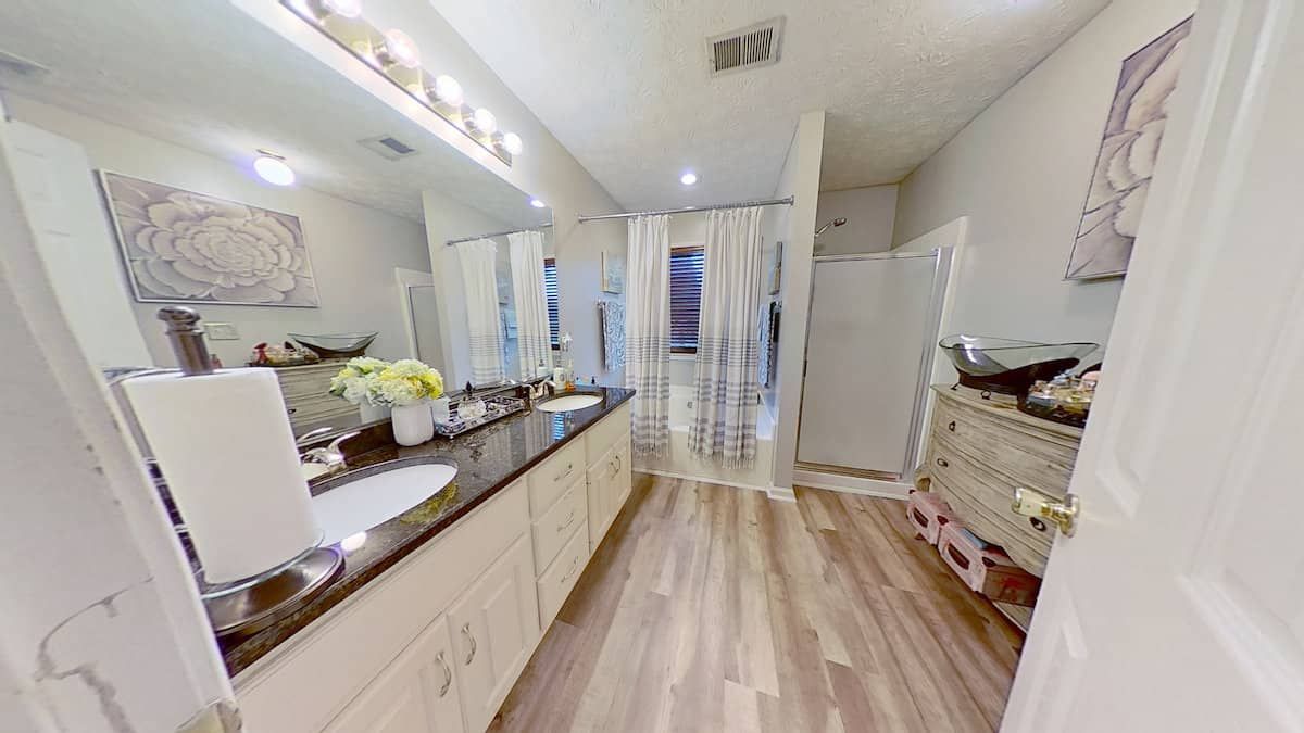 Bathroom with double sinks, light wood-look flooring, and white cabinets. A large mirror hangs above the countertop.
