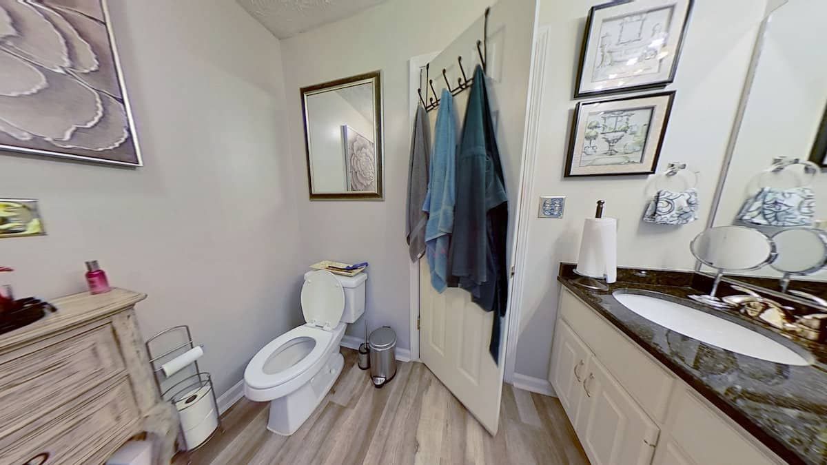 A bathroom with a toilet, vanity, and shower. Towels hang on the door and artwork is on the walls.