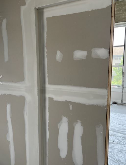 Drywall with tape and mud applied around a doorway, awaiting final finishing. Interior setting with a window visible.