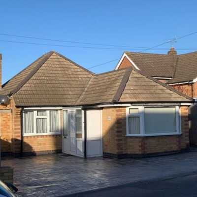 Tan brick bungalow with brown roof and white windows and door.
