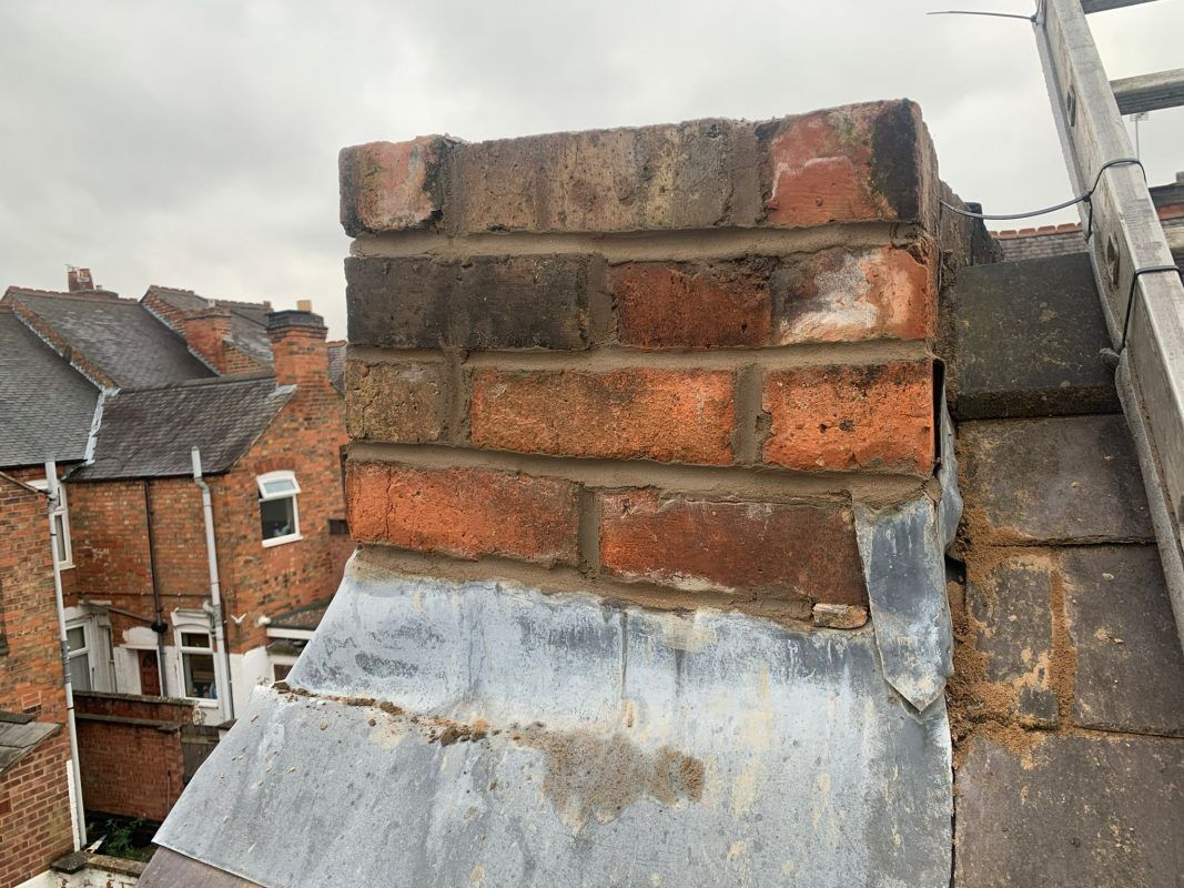 Chimney leadwork repair in Ely, showing weathered brickwork and the grey lead flashing around the chimney base.