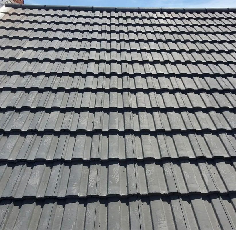A close-up view of a dark grey tiled residential roof under a clear blue sky.