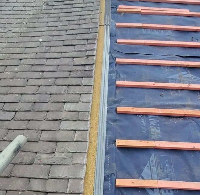 Roof with slate tiles on the left, new underlayment, and wooden supports on the right, separated by a metal flashing.