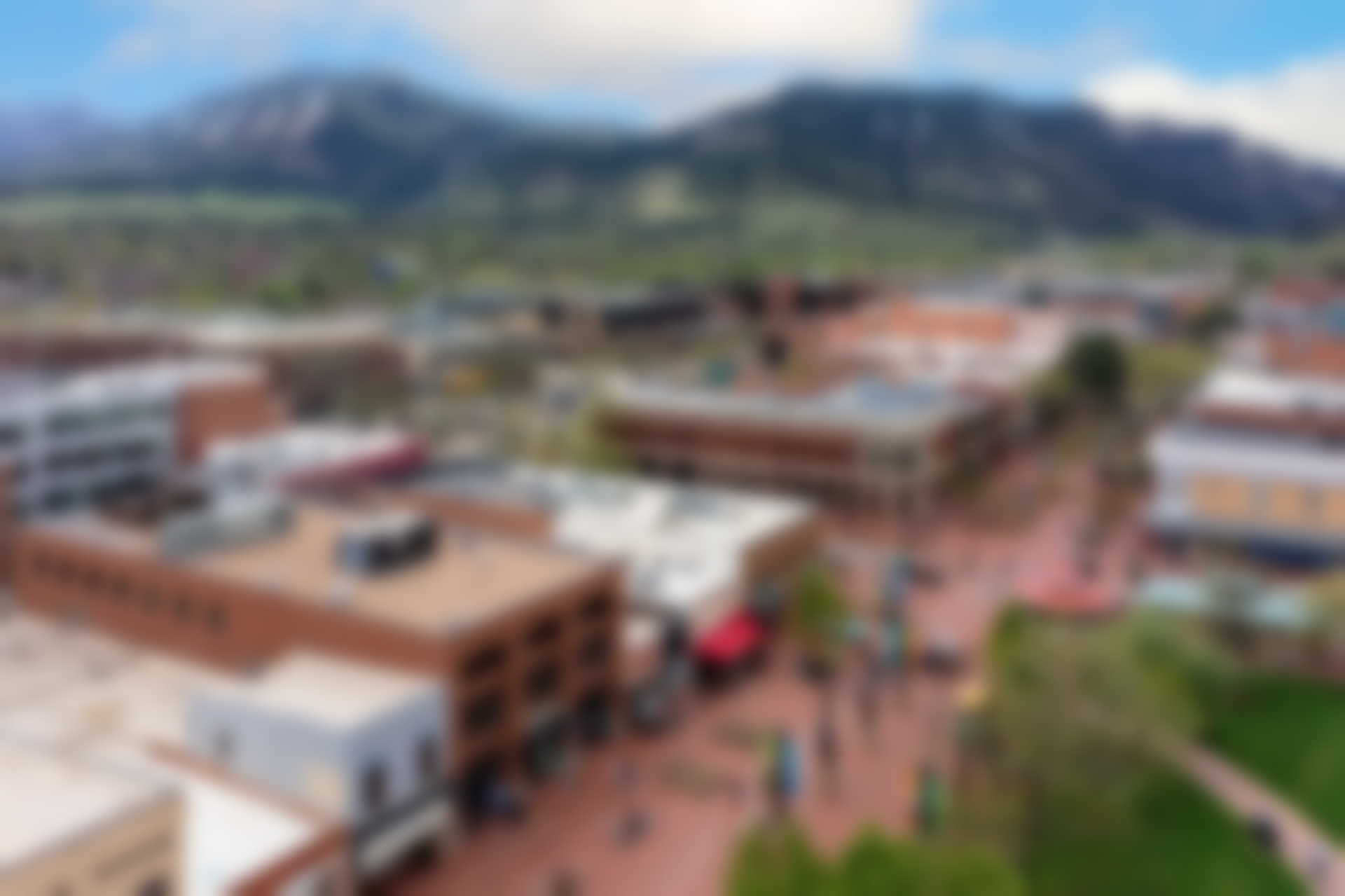 A blurred aerial view of a downtown area with brick buildings and a mountain backdrop.
