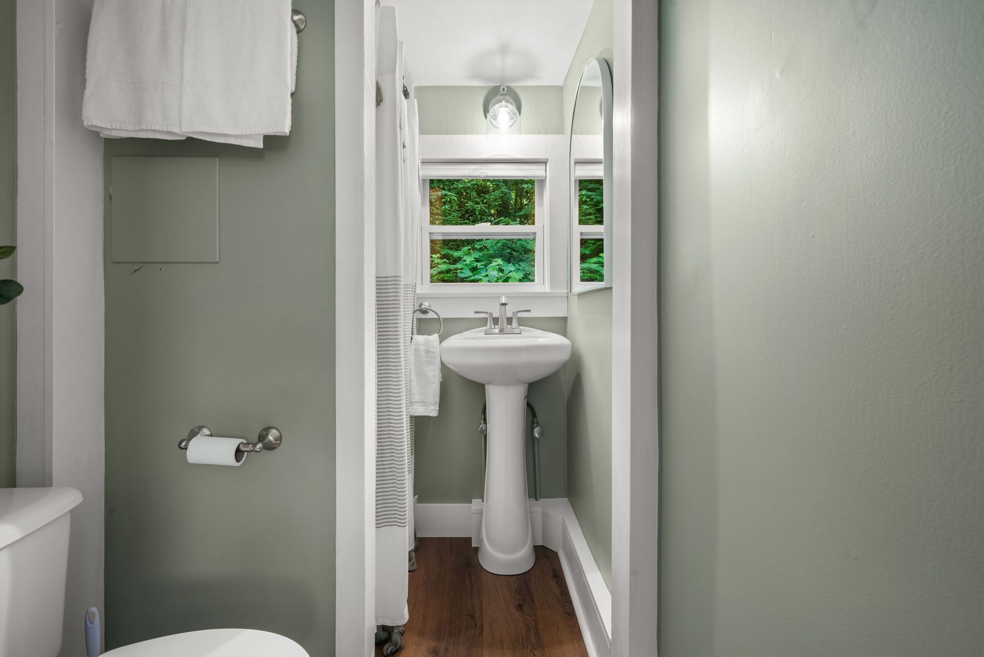 A bathroom with a toilet , sink , mirror and window.