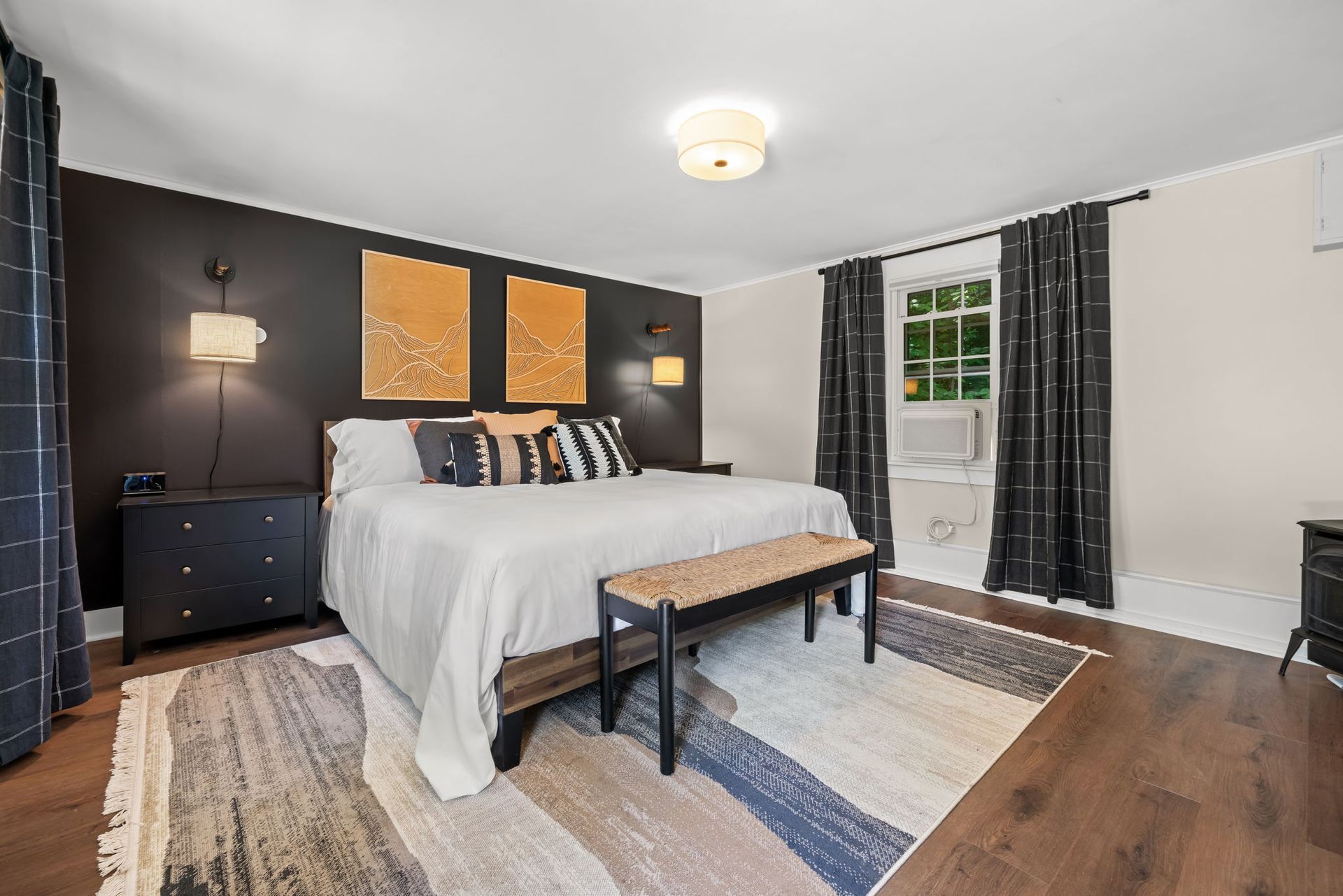 A bedroom with a large bed , dresser , nightstand , rug and window.
