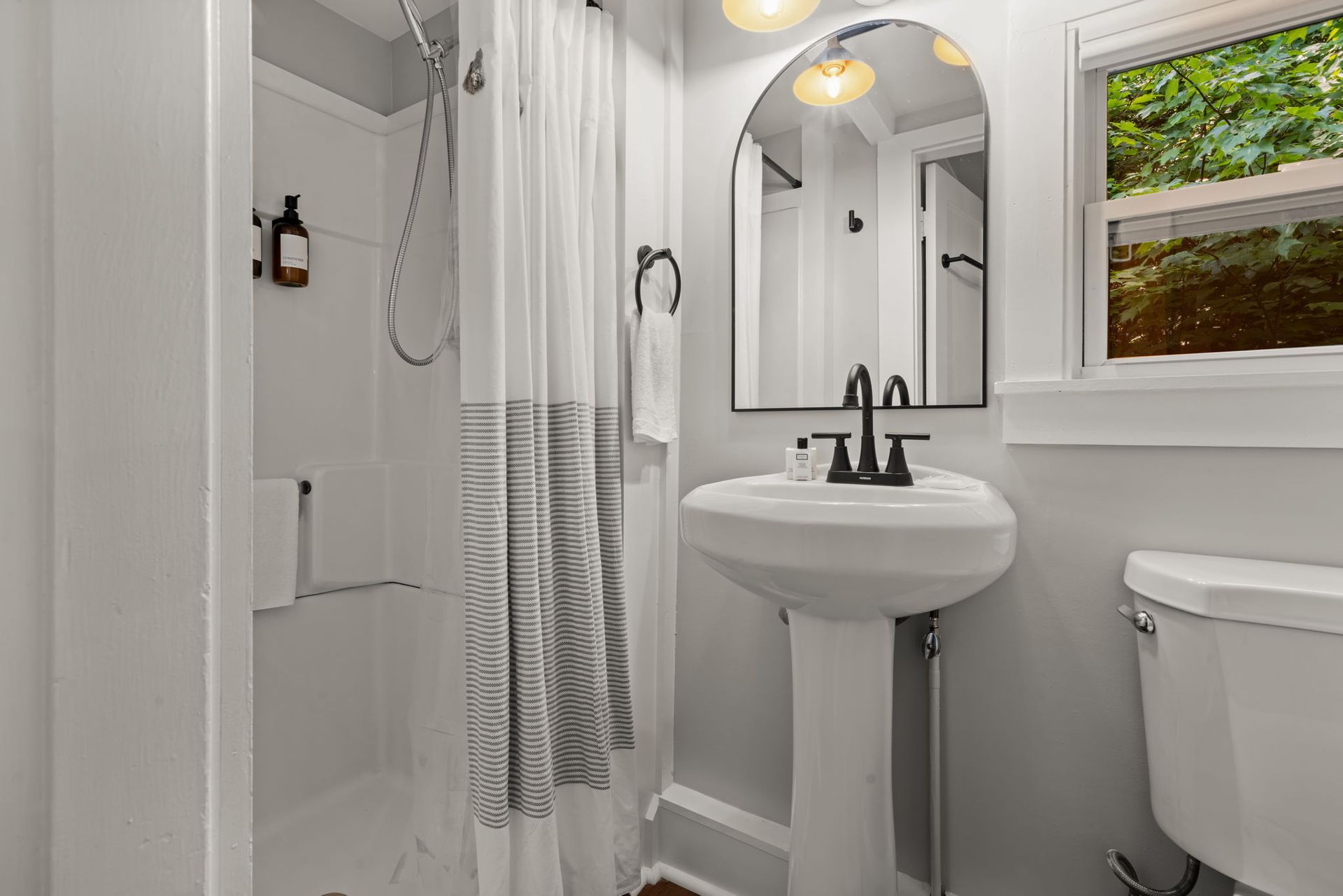 A bathroom with a sink , toilet , shower and mirror.