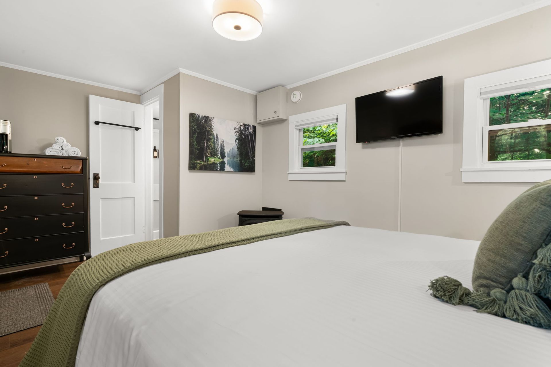 A bedroom with a bed , dresser , television and two windows.