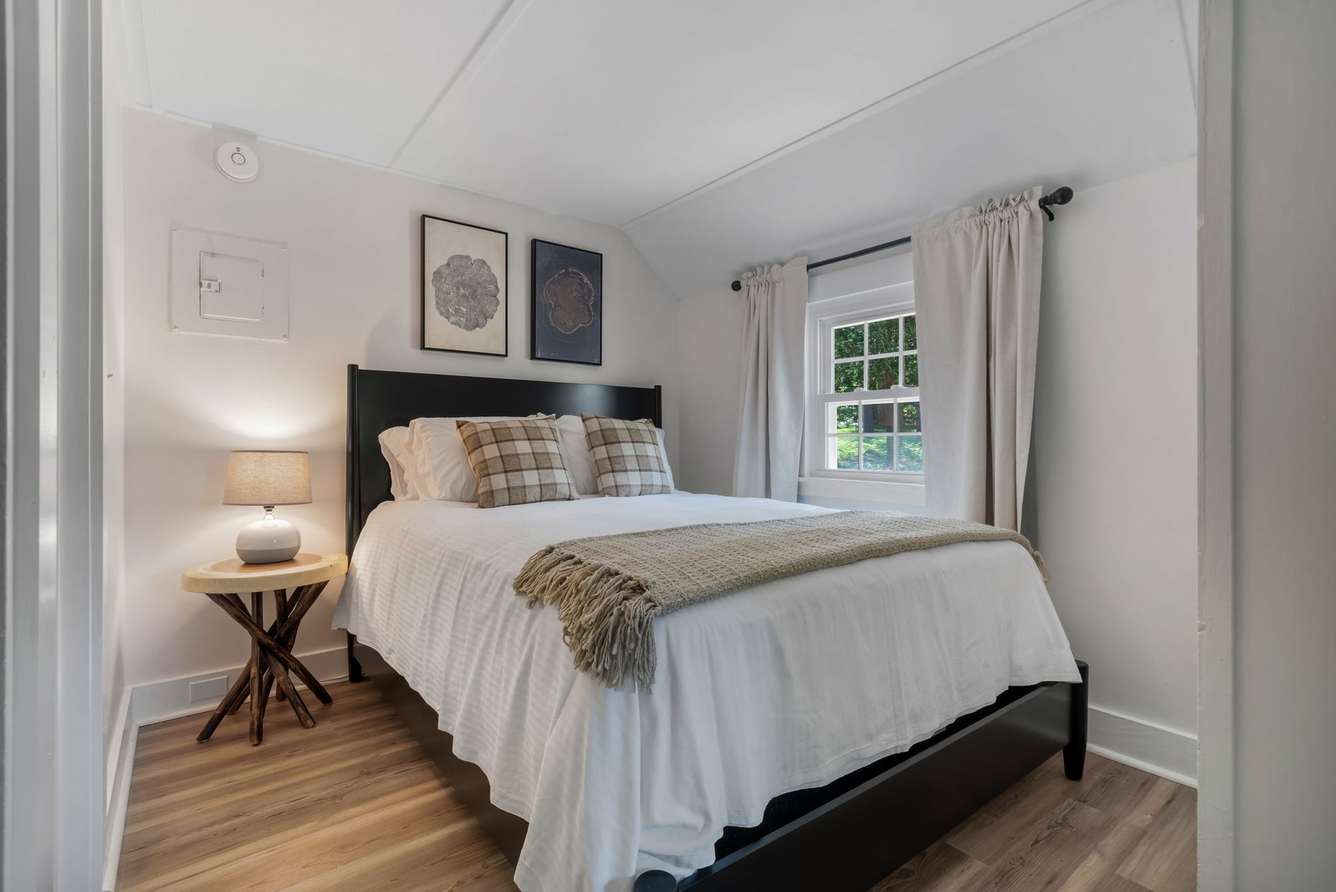 A bedroom with a bed , nightstand , lamp and window.