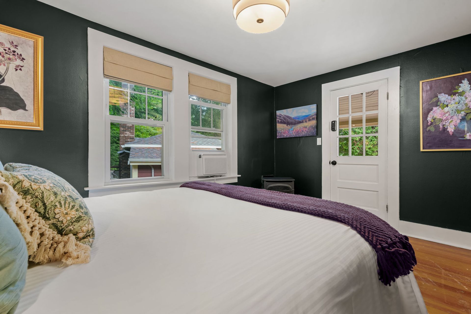 A bedroom with a bed , paintings on the wall , and a window.