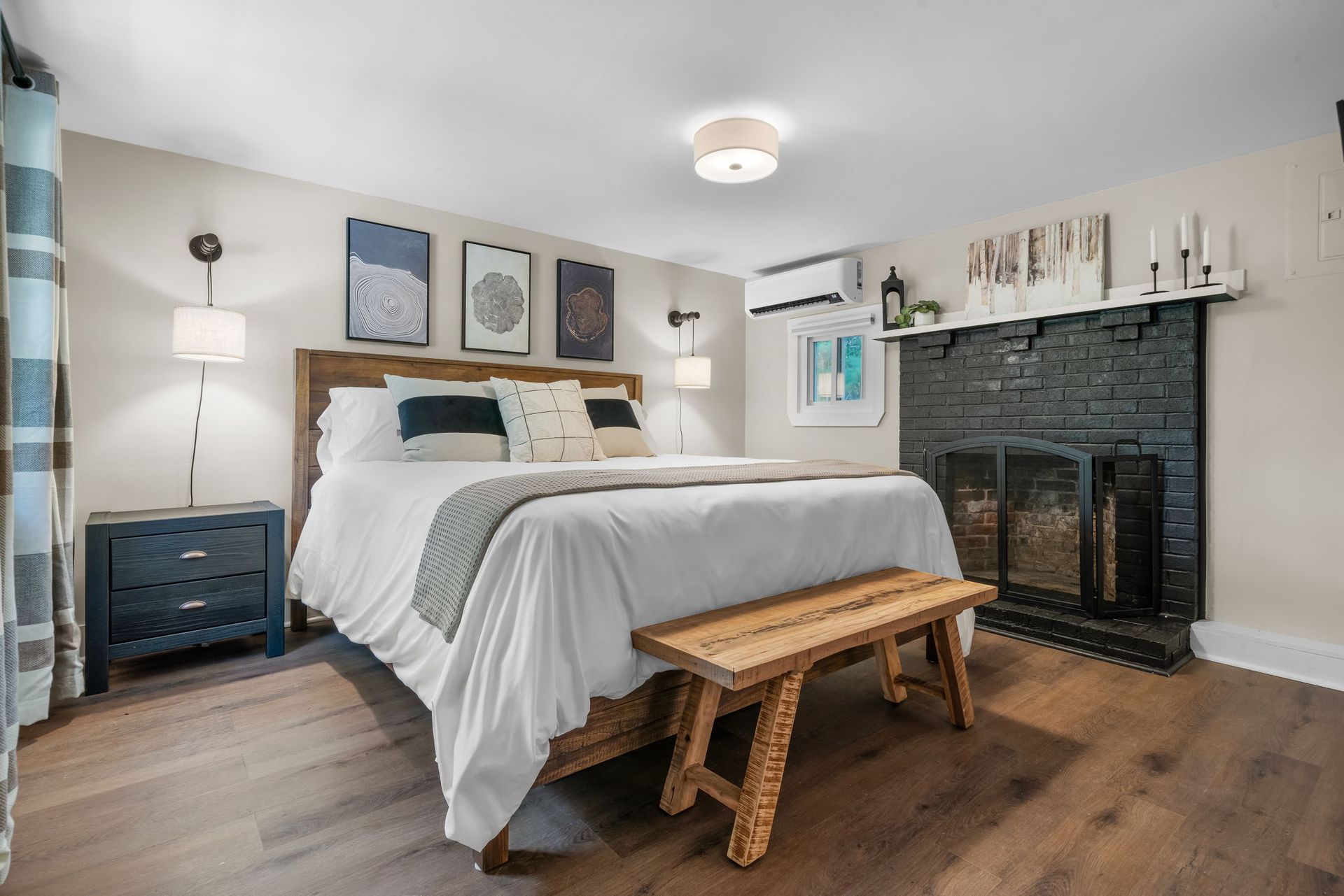 A bedroom with a bed , nightstand , bench and fireplace.