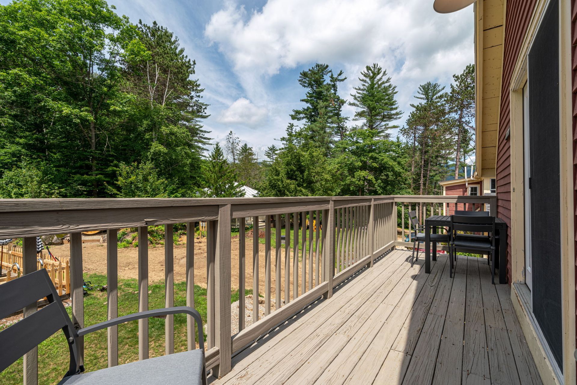 A wooden deck with a table and chairs and trees in the background.