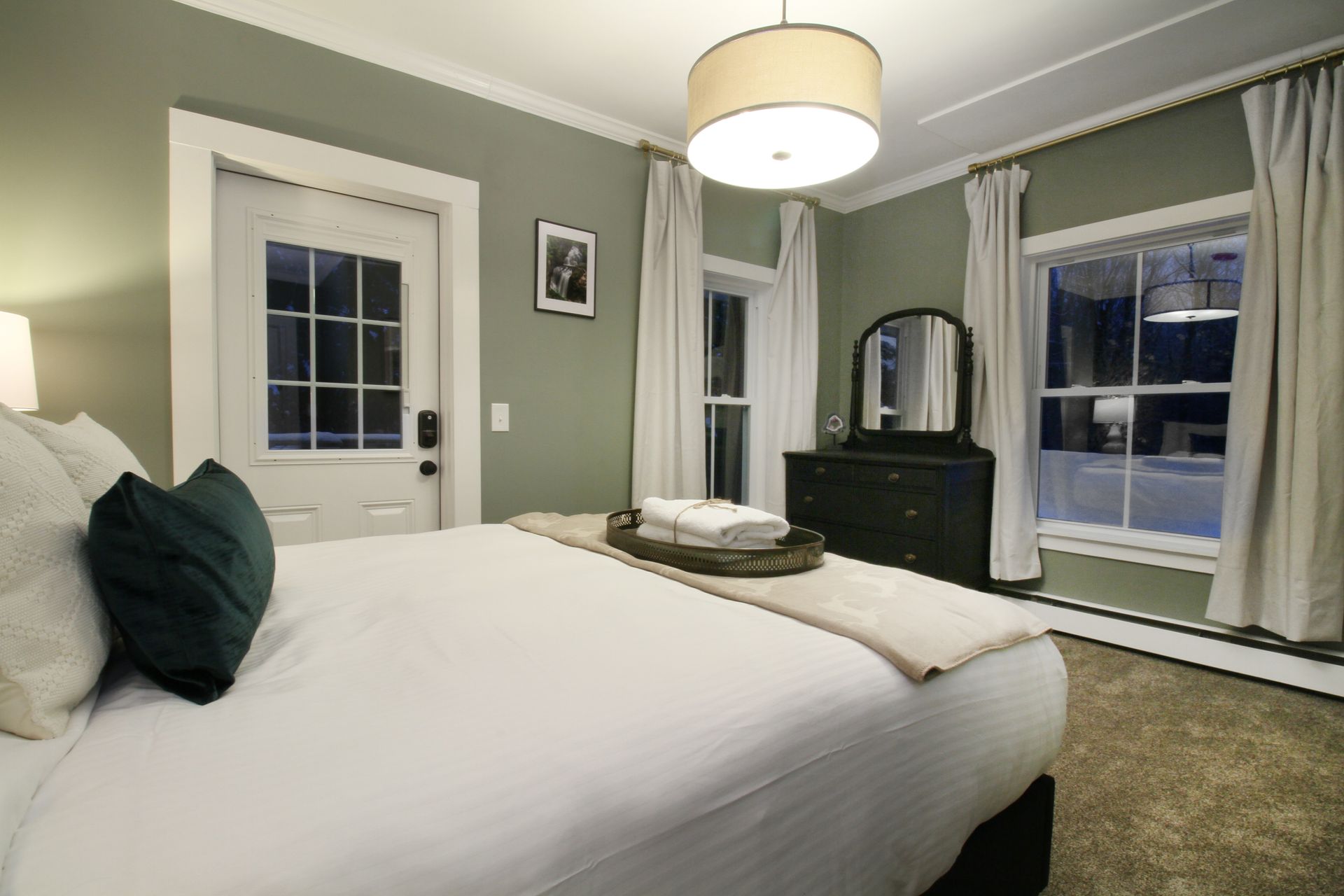 A bedroom with a bed , dresser , mirror and window.