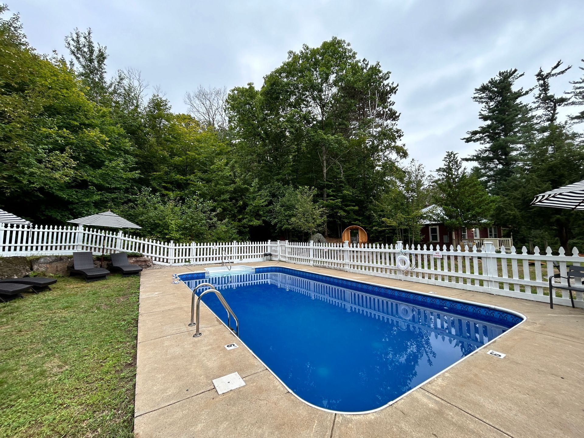A large swimming pool surrounded by a white picket fence and chairs.