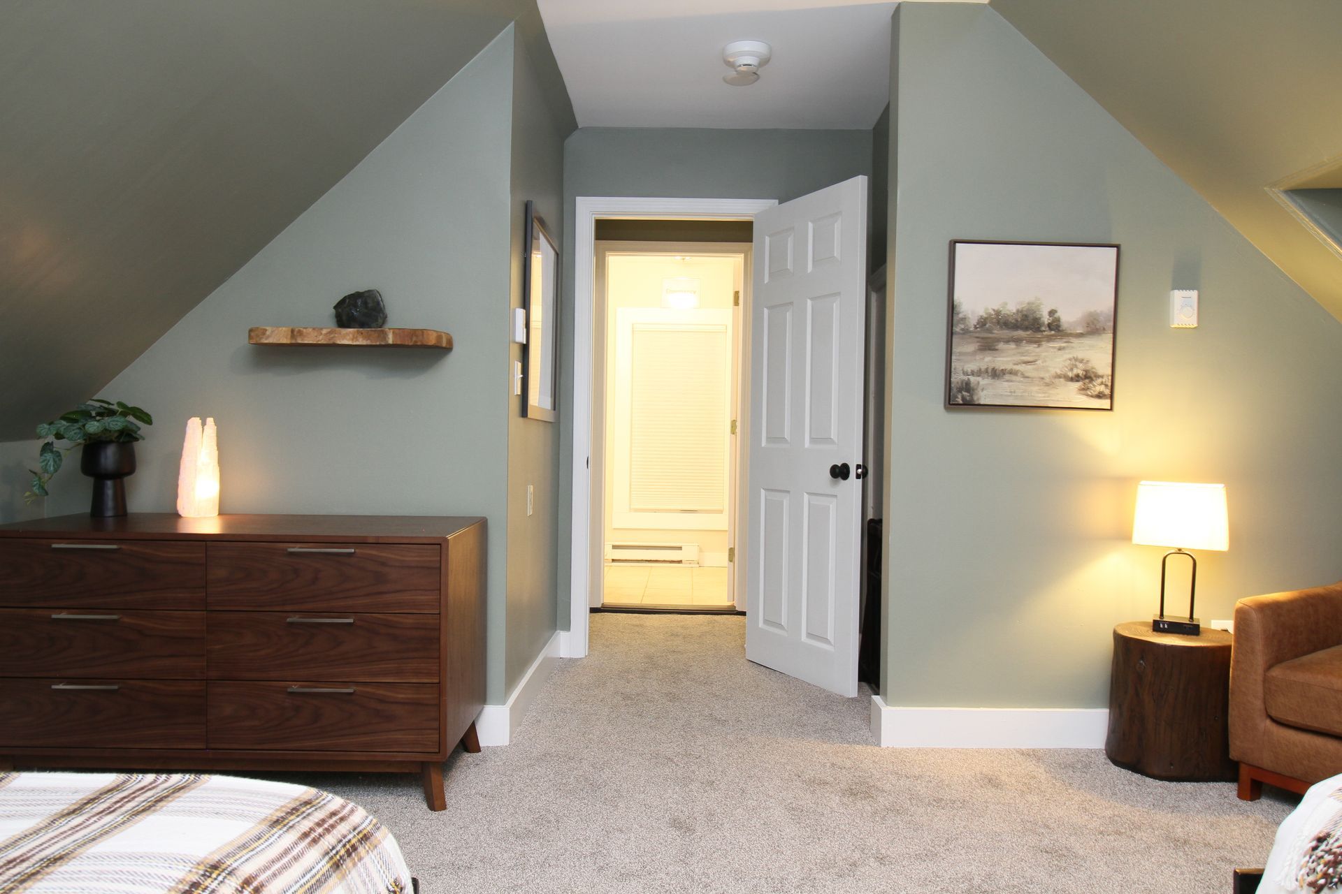 A bedroom with a bed , dresser , chair and a picture on the wall.