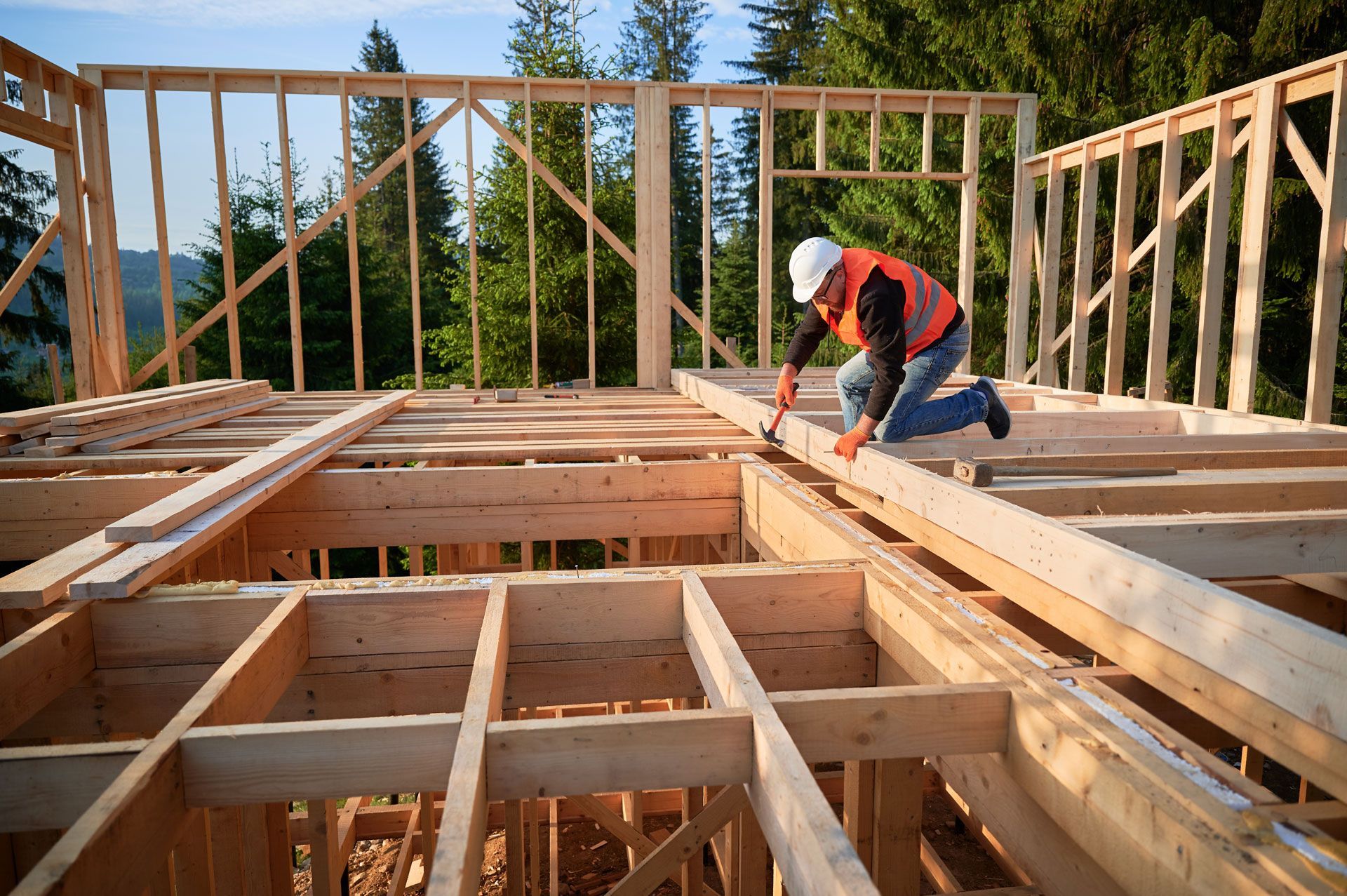 Construction worker in hard hat and vest hammering wooden beams on a building frame.