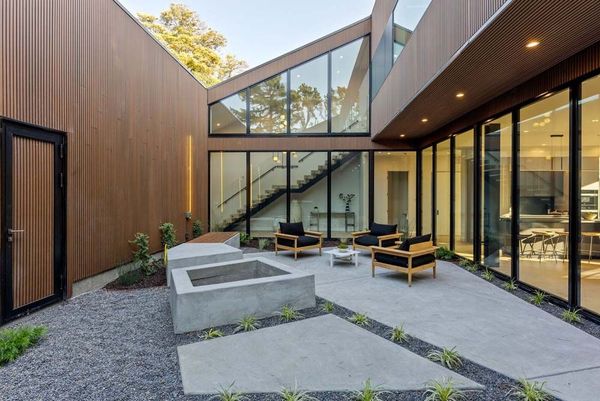 Modern home exterior with outdoor seating, glass walls, and brown siding.