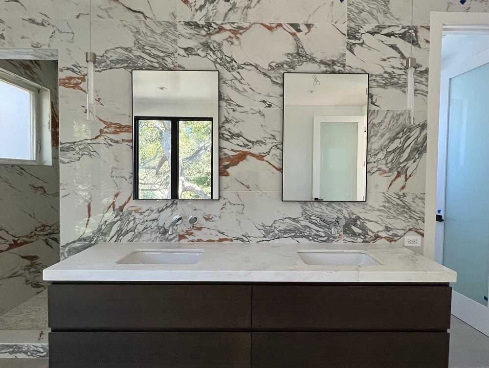 A bathroom with two sinks , two mirrors and a marble wall.