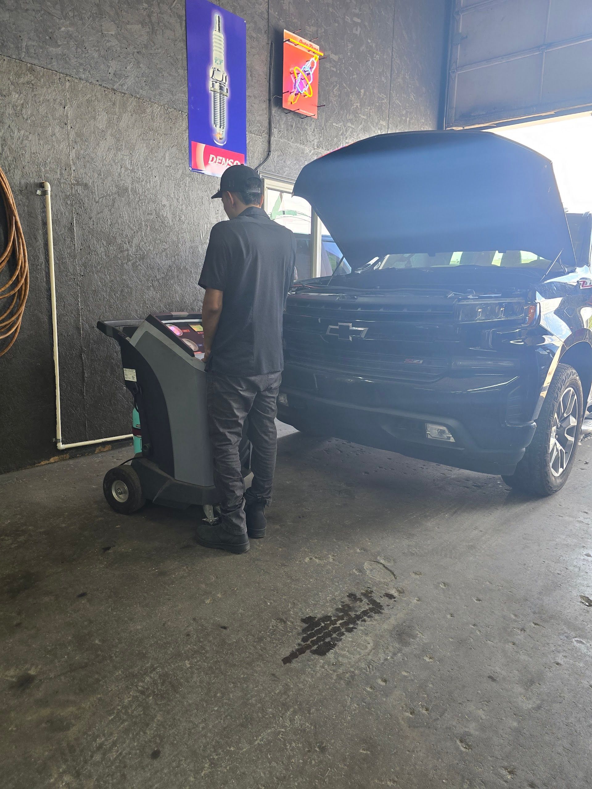 Person working beside a black car with its hood open in a garage or workshop | Kingsley Auto Service