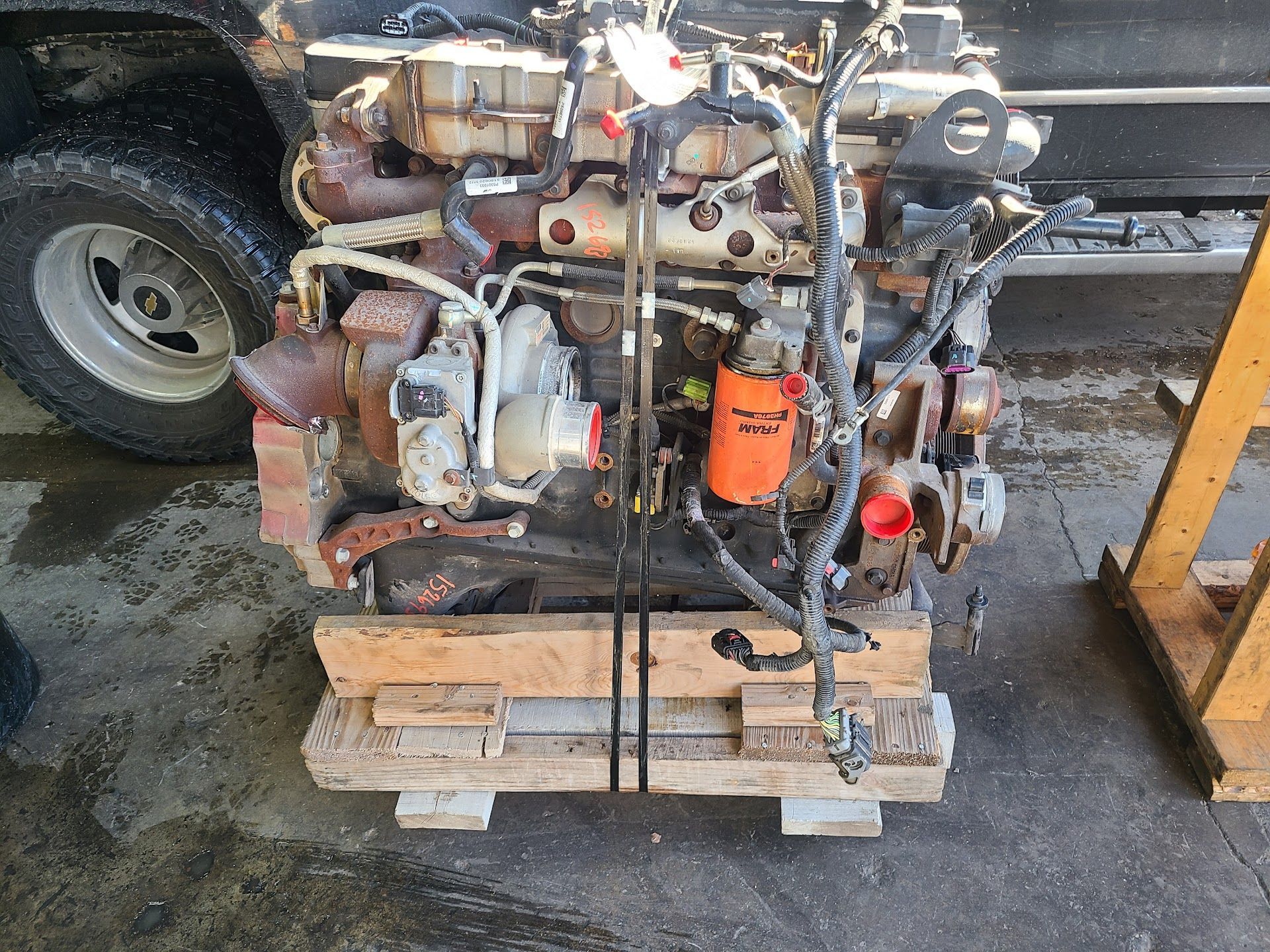 Rusty engine on a pallet with hoses and orange filter, outdoors beside a vehicle tire | Kingsley Auto Service