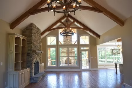 Spacious living room with stone fireplace, wood beams, and large windows.  Chandelier hangs from the vaulted ceiling.