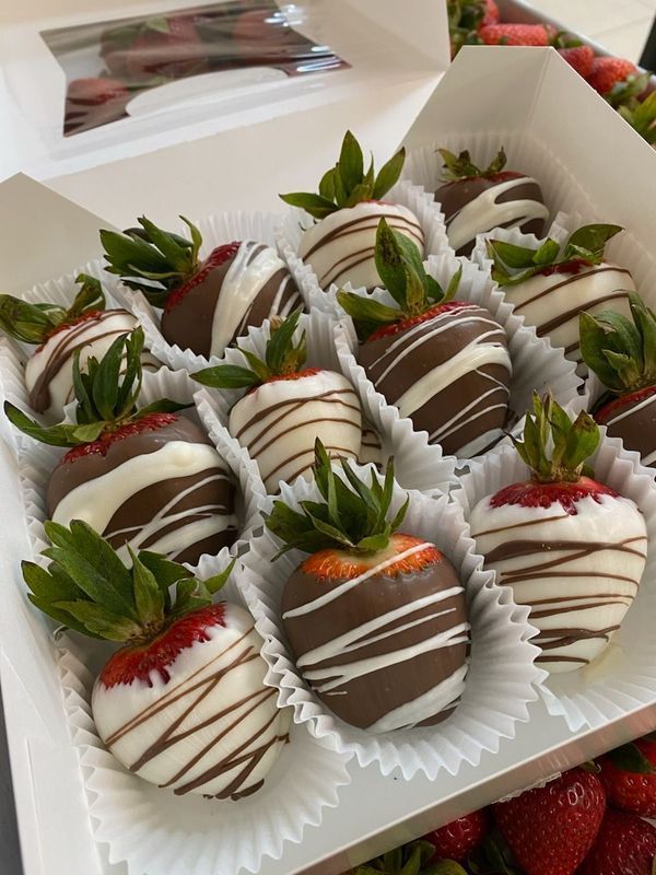 A box of fresh strawberries dipped in dark and white chocolate with decorative drizzles, sitting in individual paper liners.