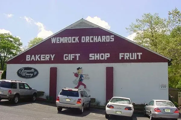 Wemrock Orchards building with a red peaked roof, bakery, gift shop, and fruit signage, with cars parked in front.