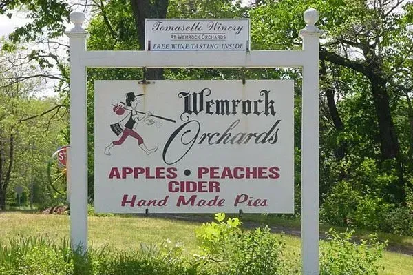 A sign for Wemrock Orchards featuring a cartoon character, advertising apples, peaches, cider, and hand-made pies.