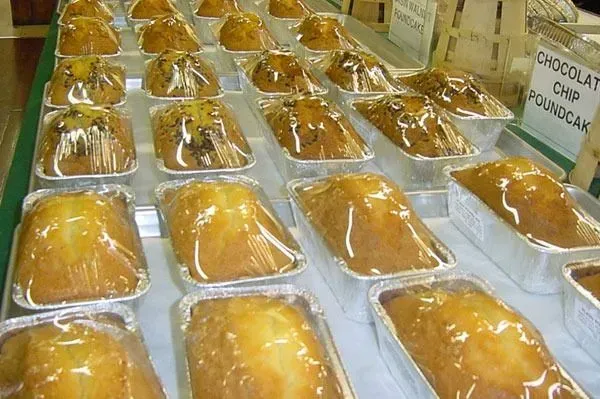 Many rectangular loaf cakes wrapped in clear plastic are arranged in rows on trays at a bakery or market stall.