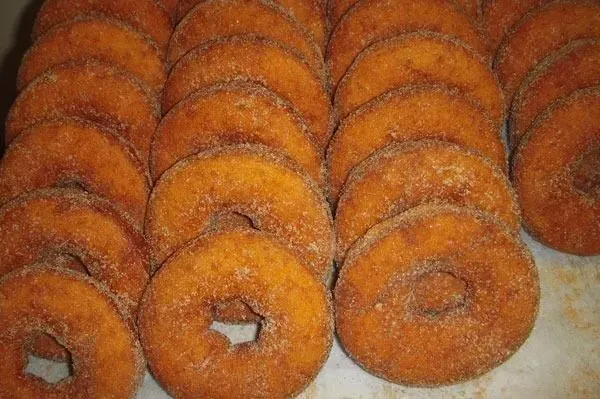 A top-down view of many golden-brown, cinnamon-sugar-coated ring donuts arranged on a white surface.