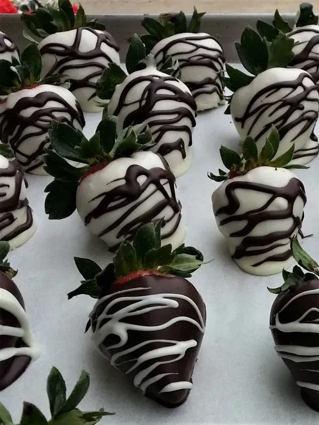 A tray of strawberries dipped in white chocolate with dark drizzle and dark chocolate with white drizzle.