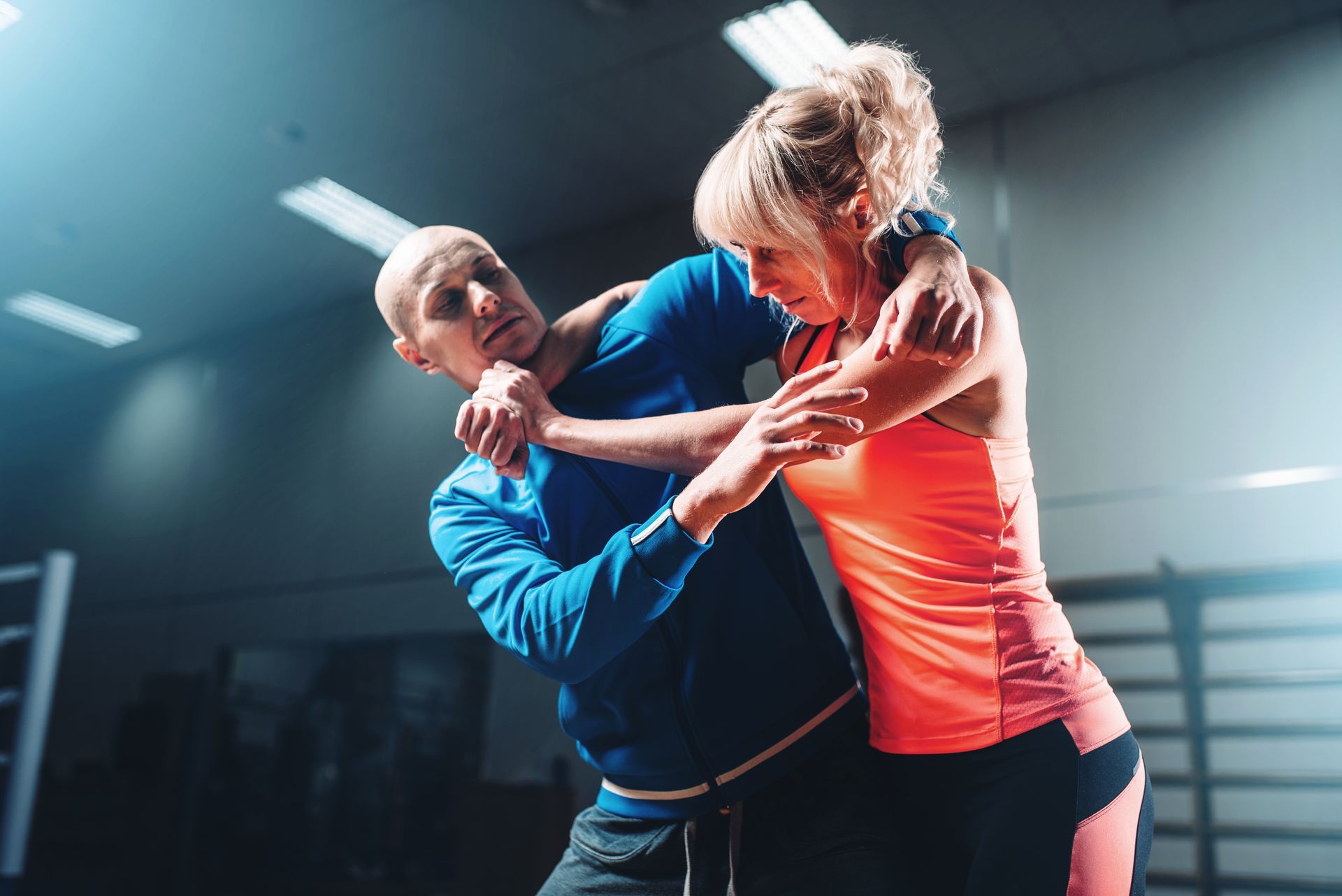 A man and a woman are practicing self defense in a gym.