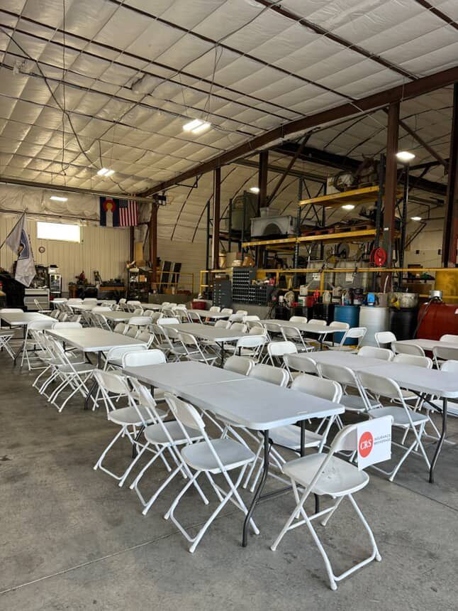 Tables and chairs set up inside a large warehouse; flags and equipment visible.