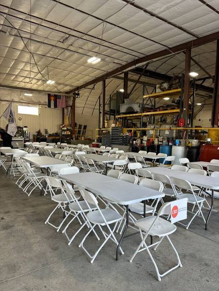 Tables and chairs set up inside a warehouse. Flags and equipment visible in the background.
