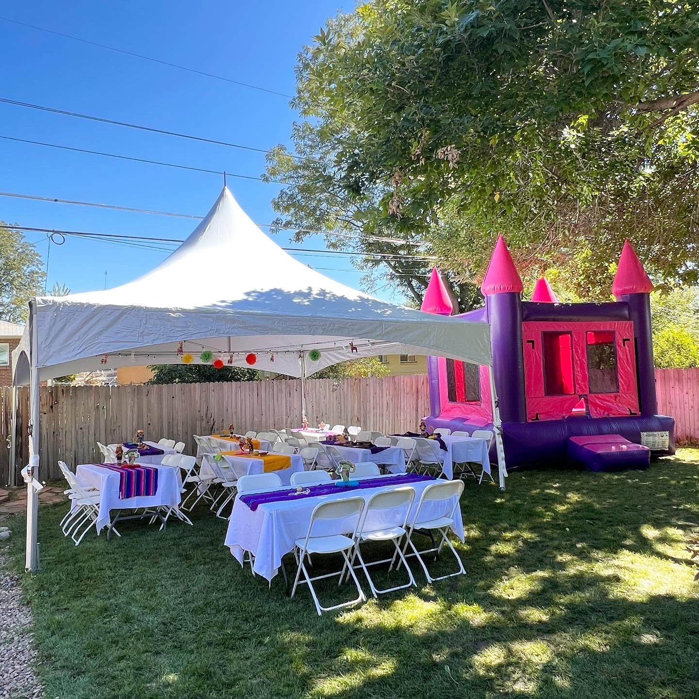Backyard party setup with tent, tables, chairs, and inflatable castle.