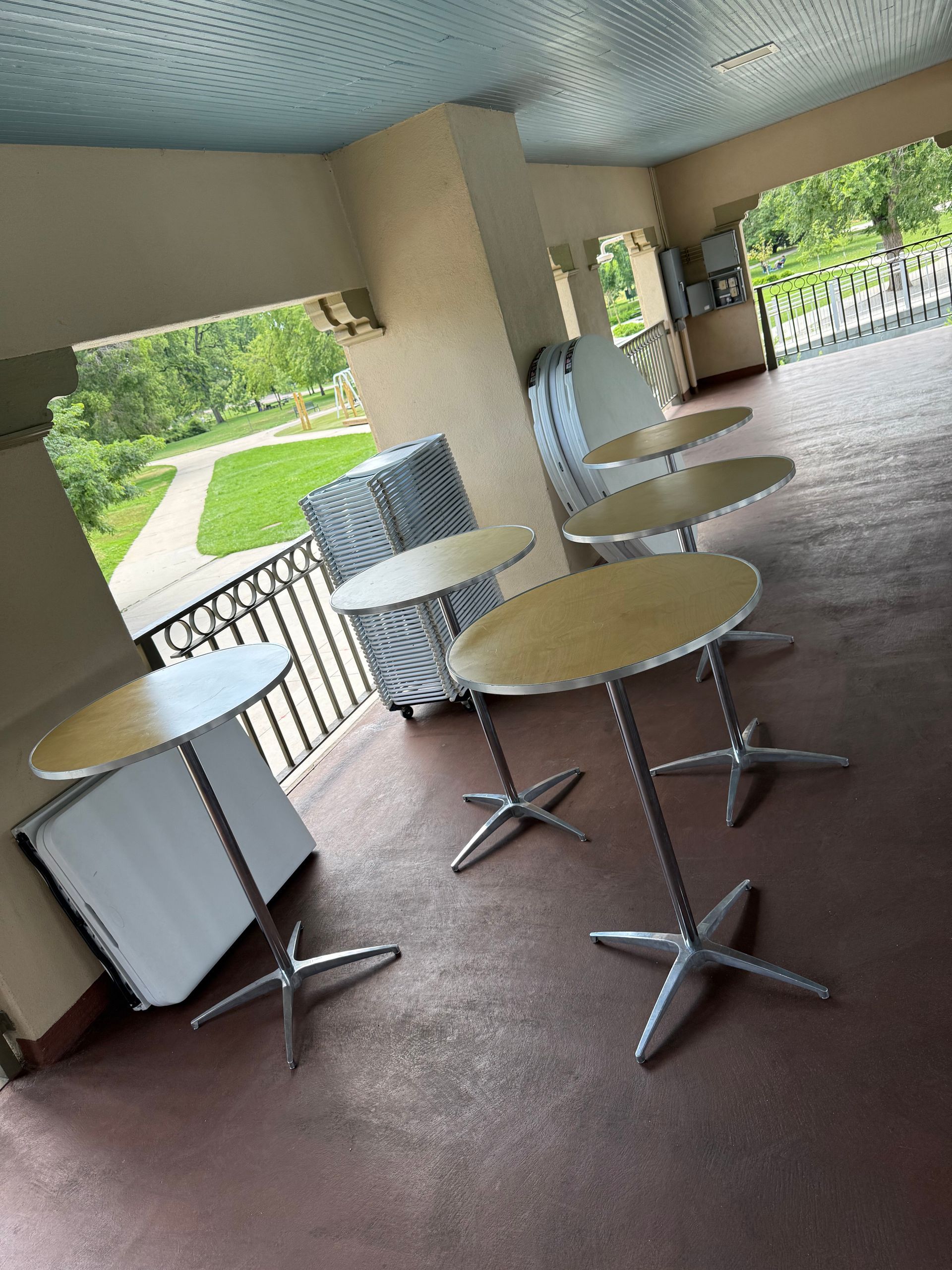 Outdoor patio with round tables and metal legs. Green lawn visible in background.