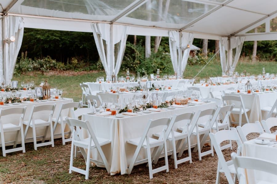 Wedding reception tent setup with white tables, chairs, and decorations.