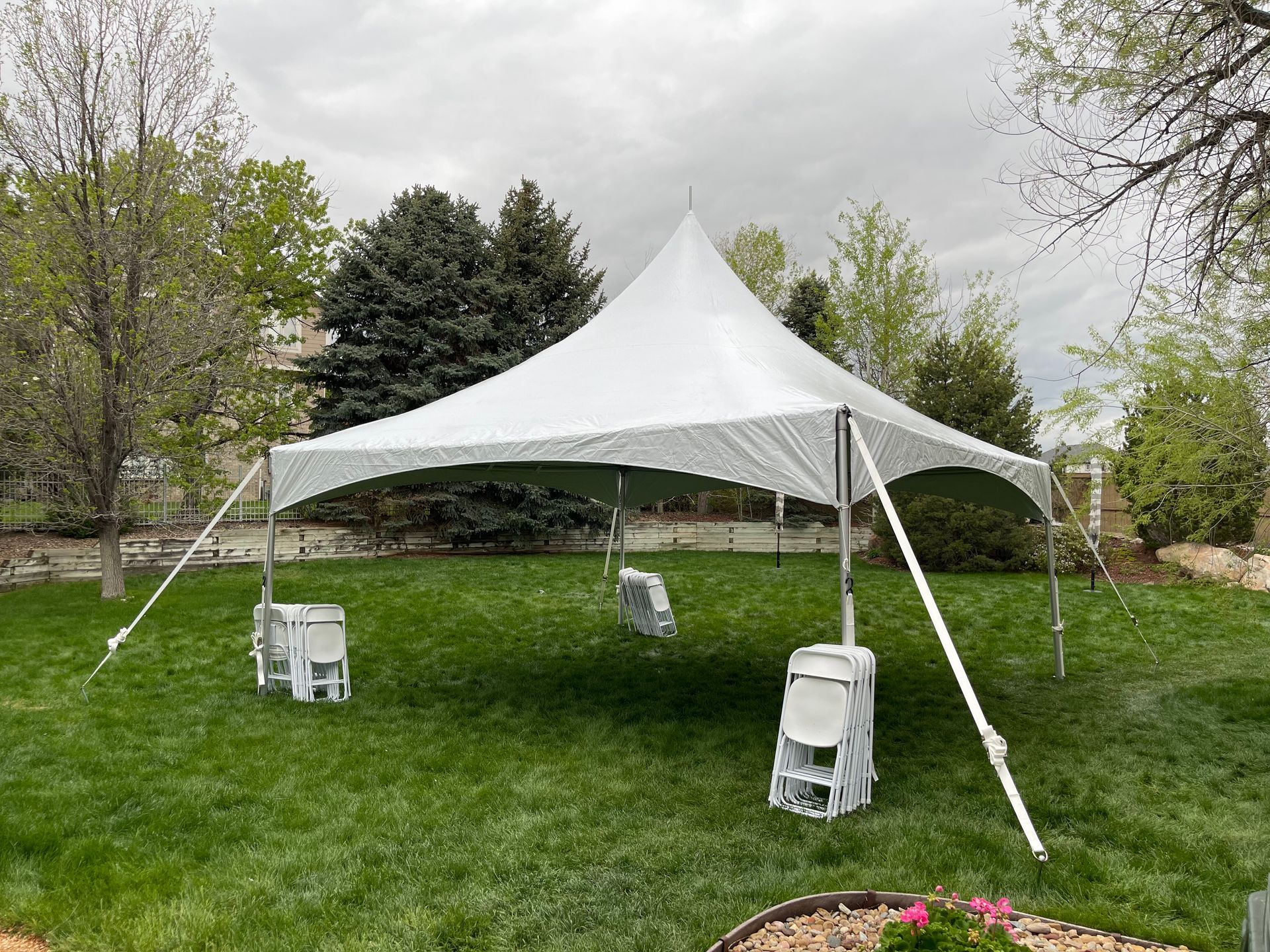 White party tent set up on green lawn with white chairs. Trees in background.