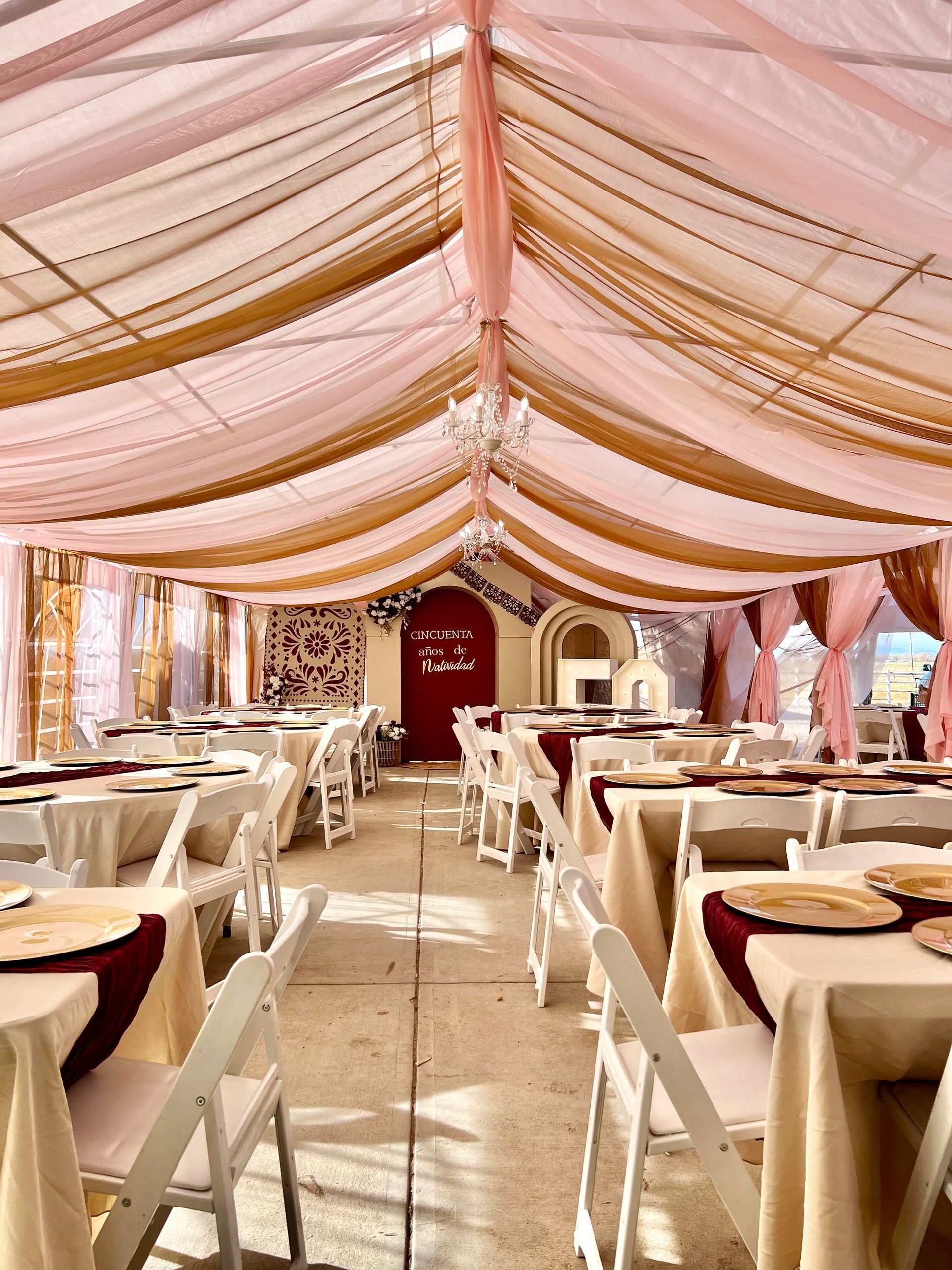 Wedding reception tent with draped ceiling, tables, and white chairs.