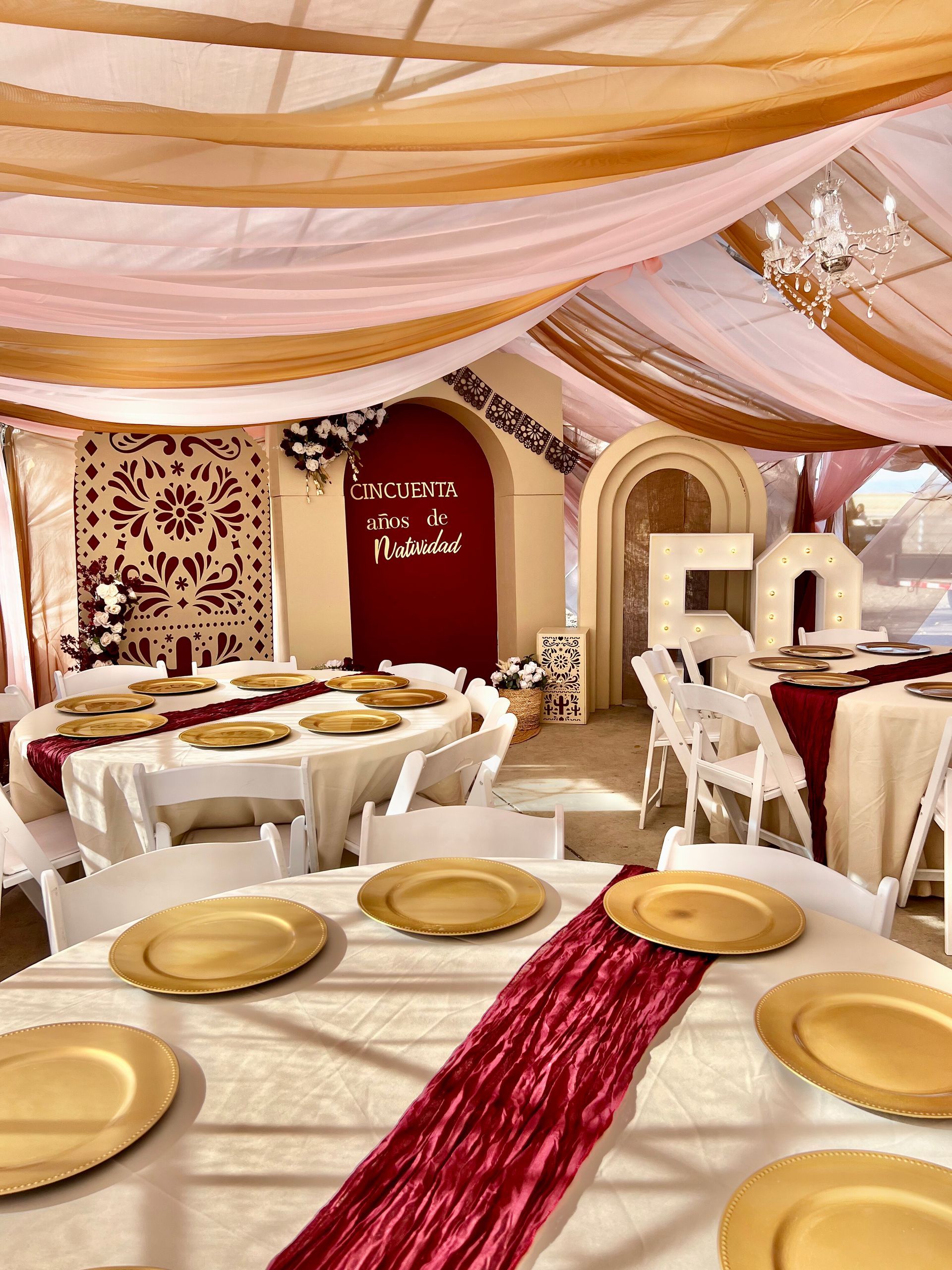 Event venue with draped fabric ceiling, round tables with gold chargers, and burgundy runners.