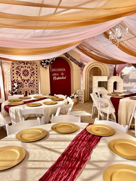 Indoor event space decorated with draped fabric, gold accents, round tables with gold chargers, and a large 